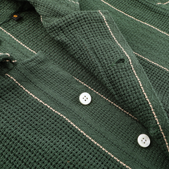 Close-up of a green crochet fabric with stripes and white buttons, likely from the Dark Green Striped Crochet Relaxed Camp Shirt by C.O.F Studio.