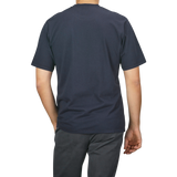 A person is standing with their back to the camera, wearing a C.O.F Studio Navy Blue Organic Cotton Crewneck T-Shirt and dark pants.