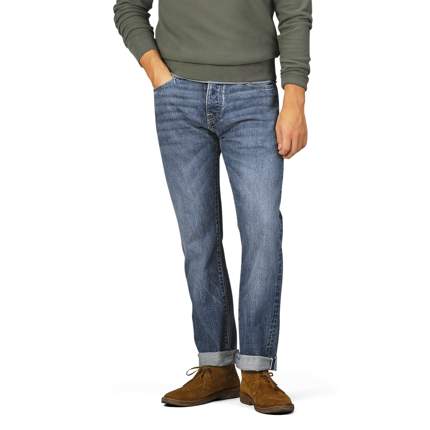 A person wearing a green long-sleeve shirt, C.O.F Studio Washed Blue 14oz Kuroki Selvedge Cotton M8 Jeans with the bottom cuffs rolled up, and brown shoes. Only the lower half of the body is visible.