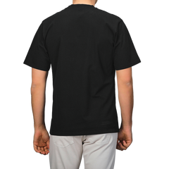 From behind, a person is wearing a C.O.F Studio Black Organic Cotton Crewneck T-Shirt with light-colored pants.