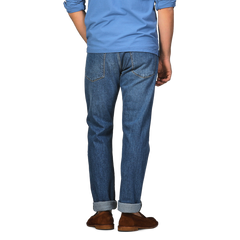 Rear view of a person in a blue shirt and brown shoes, standing with arms relaxed, showcasing C.O.F Studio's Indigo Blue Washed Organic Cotton M8 Jeans made from organic Kuroki Selvedge denim.