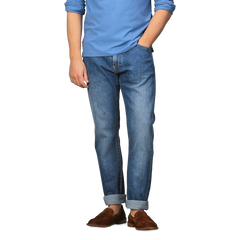 A person in a blue long-sleeve shirt, C.O.F Studio Indigo Blue Washed Organic Cotton M8 Jeans with cuffs, and brown loafers stands against a plain background.