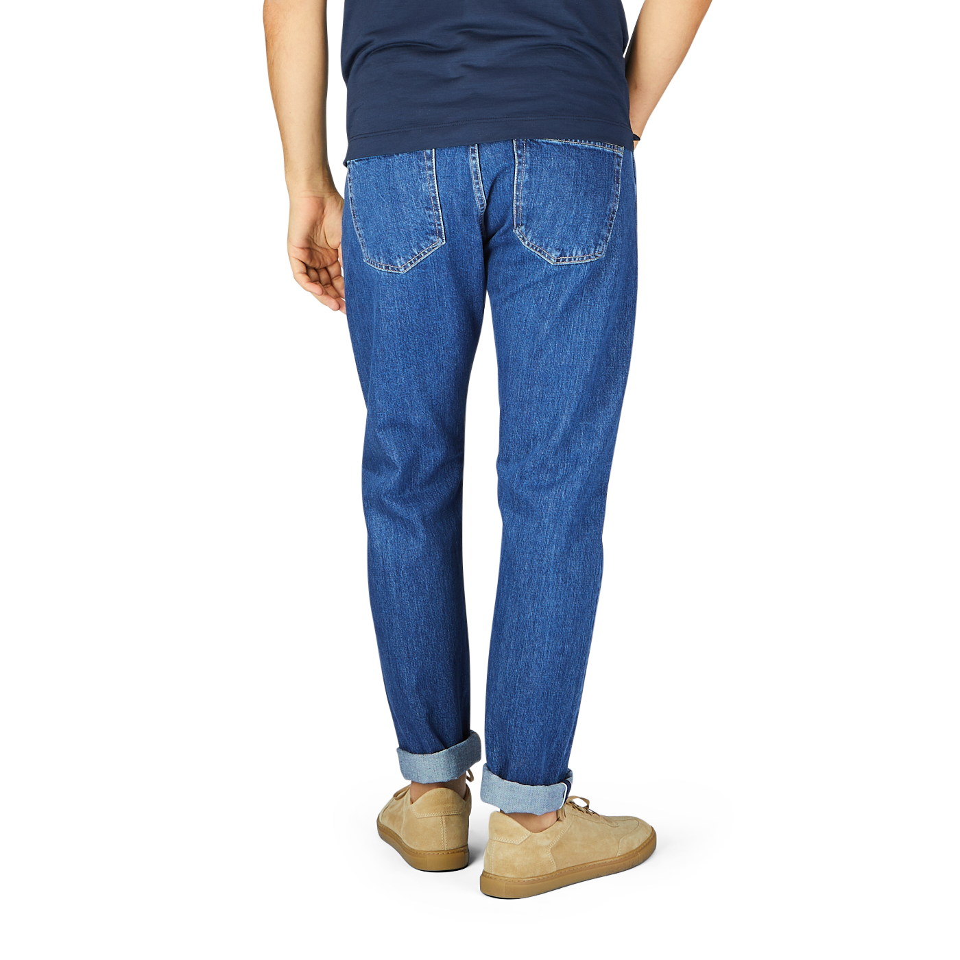 Man standing facing away, showcasing C.O.F Studio's Blue Organic Kurioki Cotton M7 6x Wash Jeans and beige shoes, with the jeans' cuffs slightly rolled up.