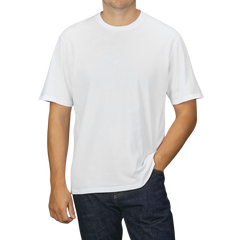 A person dressed in a C.O.F Studio White Organic Cotton Crewneck T-shirt and dark jeans, standing against a neutral grey background with one hand in their pocket.