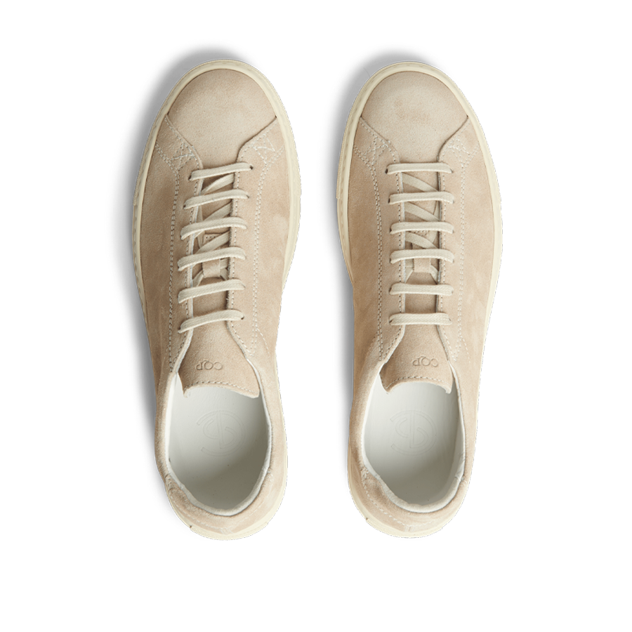 A pair of Beige Suede Leather Racquet sneakers with white laces, displayed from above on a striped background.