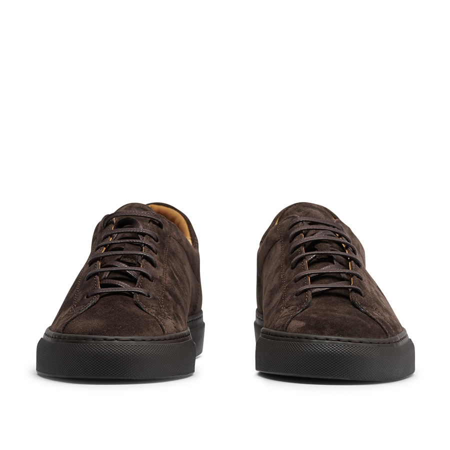 The CQP Ebony Brown Racquet Sr sneakers, made from dark brown suede calf leather with black outsoles, are viewed from the front and provide improved arch support for exceptional comfort.