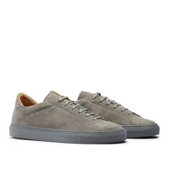 A pair of Granit Grey Suede Leather Racquet Sr Sneakers by CQP with white laces and a dark gray sole, displayed against a striped gray background.