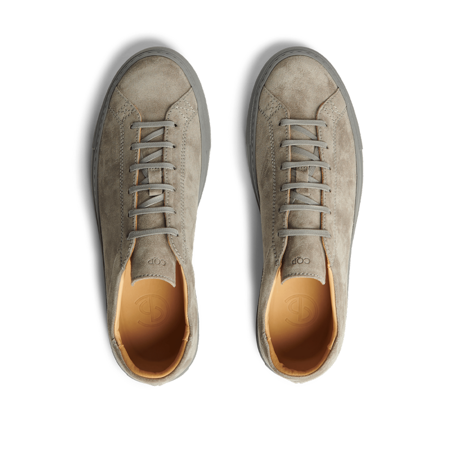 A pair of Granit Grey Suede Leather Racquet Sr sneakers by CQP with laces, viewed from above on a striped black and white background.