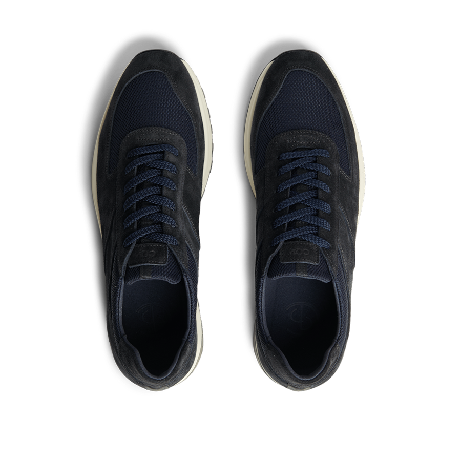 A pair of new, Obsidian Blue Suede Leather Stride Runners with laces on a striped black and white background by CQP.