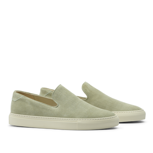 The CQP Sage Green Textured Suede Jetty Wholecut Slip-On sneakers feature a sleek slip-on design with crisp white soles, handmade in Portugal. These shoes showcase effortless style and quality craftsmanship when viewed from the side.