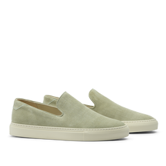 The CQP Sage Green Textured Suede Jetty Wholecut Slip-On sneakers feature a sleek slip-on design with crisp white soles, handmade in Portugal. These shoes showcase effortless style and quality craftsmanship when viewed from the side.