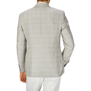Rear view of a person wearing a Canali Beige Melange Silk Wool Basketweave Blazer with white trousers on a gray background.