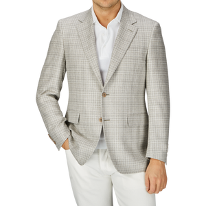 Man in a fitted beige melange silk wool basketweave blazer by Canali over a white shirt, with a partial view of white pants, standing against a grey background.