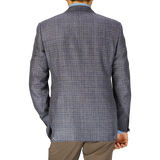 Rear view of a man wearing a Canali blue gingham checked wool silk linen blazer and beige trousers, standing against a plain background.