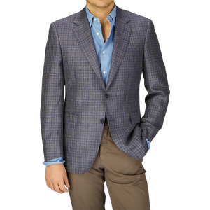 A man in a Canali Blue Gingham Checked Wool Silk Linen Blazer and light blue shirt paired with beige trousers, cropped at the chest, against a grey background.