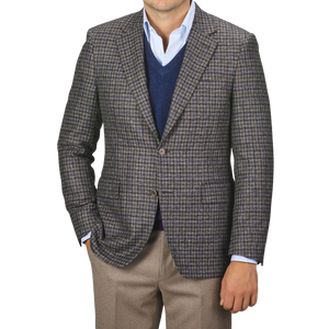 A man wearing a Canali Brown Gunclub Check Wool Drop 6 Blazer over a blue sweater and light blue shirt, paired with khaki pants, stands with one hand in his pocket.