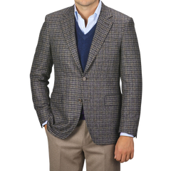 A man wearing a Canali Brown Gunclub Check Wool Drop 6 Blazer over a blue sweater and light blue shirt, paired with khaki pants, stands with one hand in his pocket.