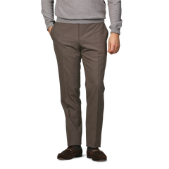 Wearing Canali's Brown Matte Wool Flat Front Trousers, a gray sweater, and brown loafers, a person poses with one hand in their pocket against a light gray backdrop.