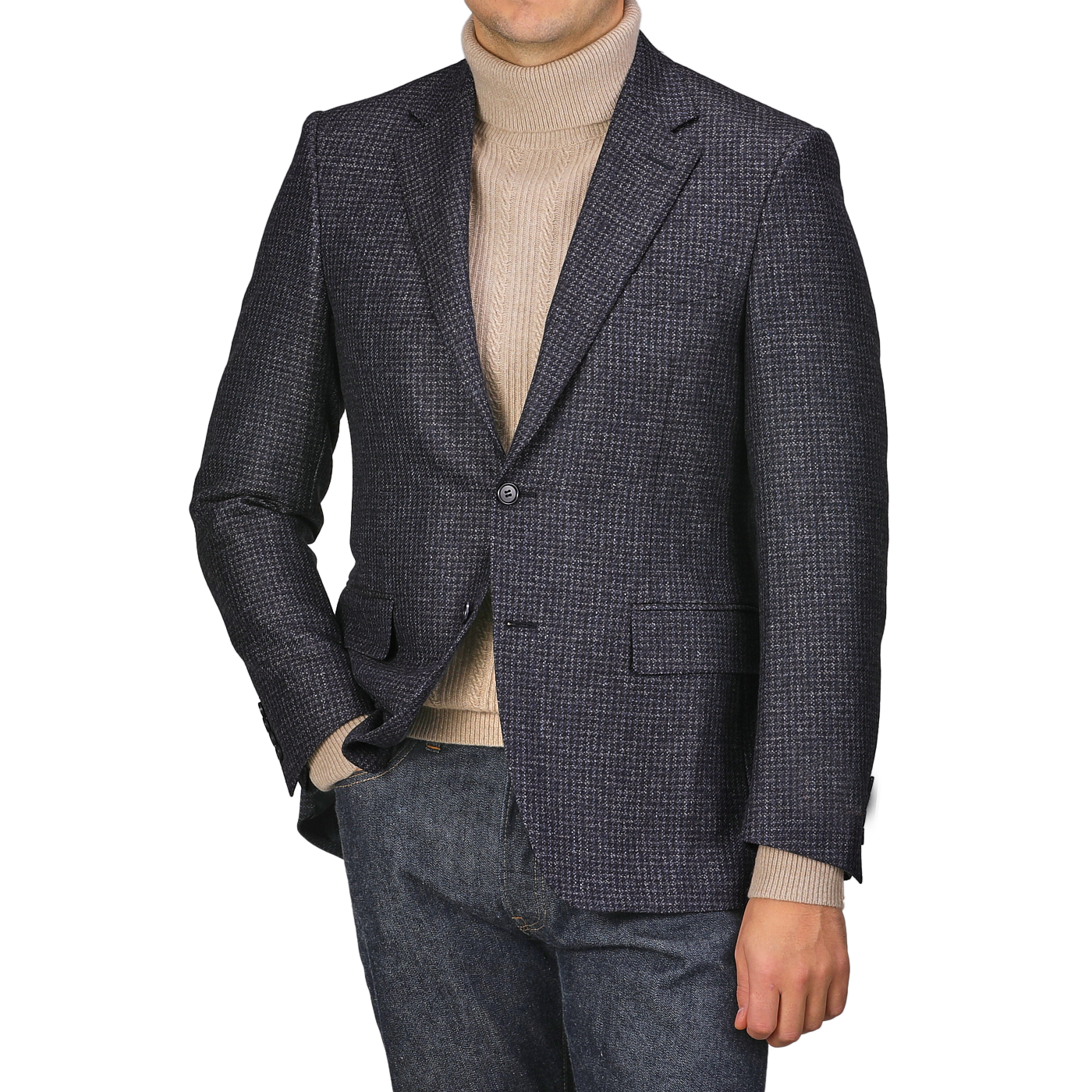 Wearing a Canali Dark Blue Checked Wool Drop 6 Blazer and a tan turtleneck, an individual stands with one hand in the pocket of their jeans against a plain background.