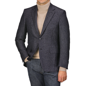 Wearing a Canali Dark Blue Checked Wool Drop 6 Blazer and a tan turtleneck, an individual stands with one hand in the pocket of their jeans against a plain background.