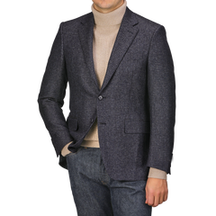 Wearing a Canali Dark Blue Checked Wool Drop 6 Blazer and a tan turtleneck, an individual stands with one hand in the pocket of their jeans against a plain background.