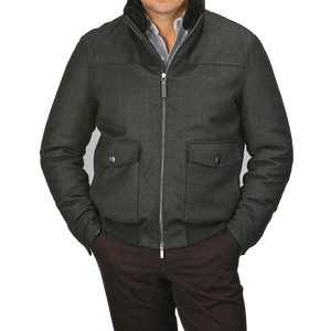 A person wearing a Canali dark green bomber jacket with a wool fur collar and two front pockets stands against a plain gray background.