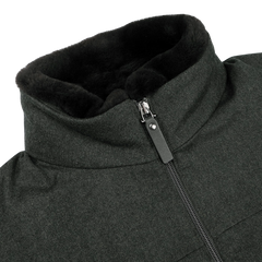 Close-up of a dark green bomber jacket with a high collar and zipper. The collar, lined with black faux fur, is detachable for versatility. Made by Canali, the wool exterior adds elegance while being rain-resistant, ensuring style and function in any weather.