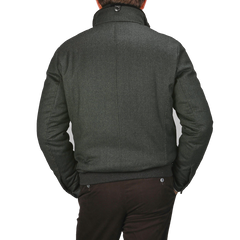 A person wearing a Canali dark green wool fur collar bomber jacket with hands in pockets, viewed from behind, highlights its elegant exterior.