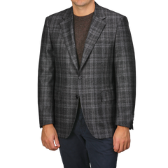 A person wearing a Canali Dark Grey Checked Wool Silk Drop 6 Blazer, a brown sweater, and navy pants stands against a plain background.