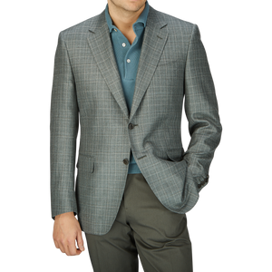 Man wearing a stylish Canali Green Checked Wool Silk Linen Blazer over a teal shirt, paired with dark trousers, against a plain background.