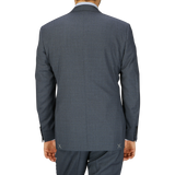Rear view of a man wearing a full canvas construction Canali Grey-Blue Melange Wool Suit jacket and pants, standing against a light grey background.