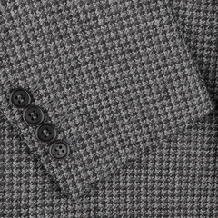 Close-up of the Canali Grey Dogtooth Wool Drop 6 Blazer fabric, featuring a folded edge and showcasing four black buttons arranged in a line, ideal for crafting a sophisticated dark grey blazer.