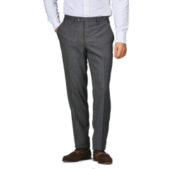 A person wearing Canali Grey Melange Wool Flat Front Trousers, a white shirt, and brown shoes stands with one hand in their pocket.