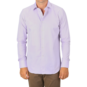 A man wearing a Canali Lilac Cotton Herringbone Single Cuff Shirt and brown pants stands facing forward, with only part of his face visible.