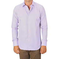 A man wearing a Canali Lilac Cotton Herringbone Single Cuff Shirt and brown pants stands facing forward, with only part of his face visible.