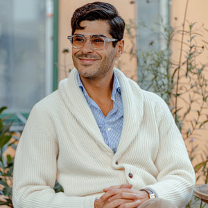 A man wearing an Ecru Beige Lambswool Shawl Collar Cardigan by William Lockie and sunglasses made of Scottish lambswool.