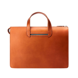 The Carl Friedrik Cognac Vachetta Leather Vallance Slim Briefcase is a streamlined accessory featuring a handle and zippered top closure, crafted from premium Italian vachetta leather against a plain background.