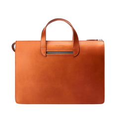 The Carl Friedrik Cognac Vachetta Leather Vallance Slim Briefcase is a streamlined accessory featuring a handle and zippered top closure, crafted from premium Italian vachetta leather against a plain background.