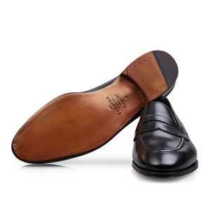 A single Carmina black calf leather Uetam penny loafer lying on its side with the sole facing up.