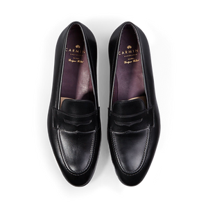 A pair of Carmina black calf leather Uetam penny loafers against a black background.