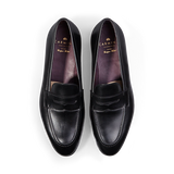 A pair of Carmina black calf leather Uetam penny loafers against a black background.