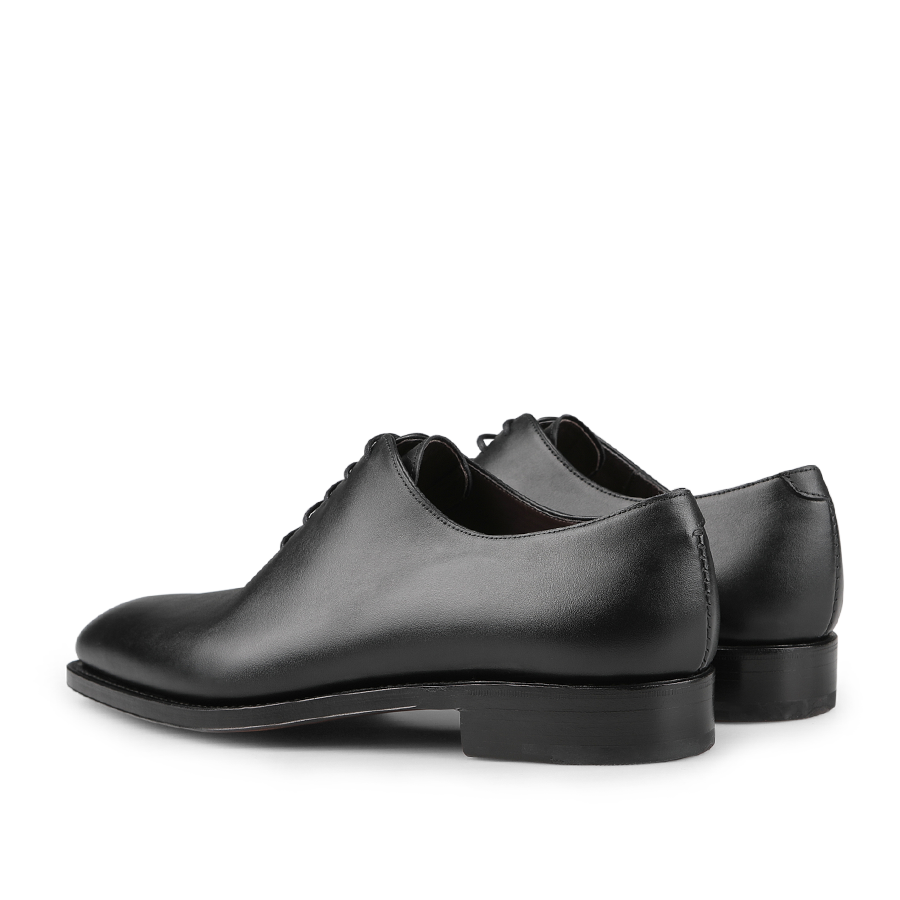 A pair of Black Calf Leather Wholecut Rain Oxford Shoes from Carmina is elegantly displayed at an angle, highlighting their polished finish and simple design. Featuring Goodyear welted construction, these timeless classics promise durability and style.