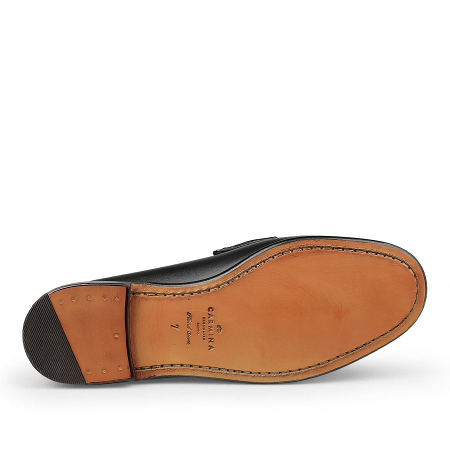 The image highlights the sole of the Black Funchal Leather Xim Horsebit Loafers from Carmina, featuring beige leather and stitching, along with a brand logo and size marking.