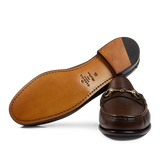 A pair of brown Carmina leather Xim horsebit loafers with gold-tone hardware, placed against a transparent background.