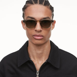 A person with braided hair wearing Chimi Model 01 Green Gradient Lenses Sunglasses 46mm with UV protection and a black zip-up shirt.
