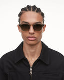 A person with braided hair wearing Chimi Model 01 Green Gradient Lenses Sunglasses 46mm with UV protection and a black zip-up shirt.