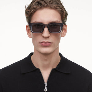 A young man wearing Chimi Model 05 Dark Grey Gradient Lenses Sunglasses 48mm and a black zippered polo shirt against a white background.