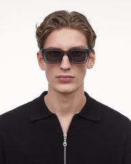 A young man wearing Chimi Model 05 Dark Grey Gradient Lenses Sunglasses 48mm and a black zippered polo shirt against a white background.