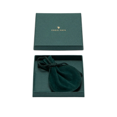 A green box embossed with "Codis Maya" contains a dainty green velvet pouch. Opening the lid reveals the pouch, offering a glimpse of the exquisite Brass Oval End Bracelet it encloses.