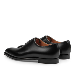 The Black Calf Leather Alex Wholecuts by Crockett & Jones feature a polished finish and laced design, highlighting their exceptional Goodyear-welted craftsmanship when viewed from the side and slightly behind.